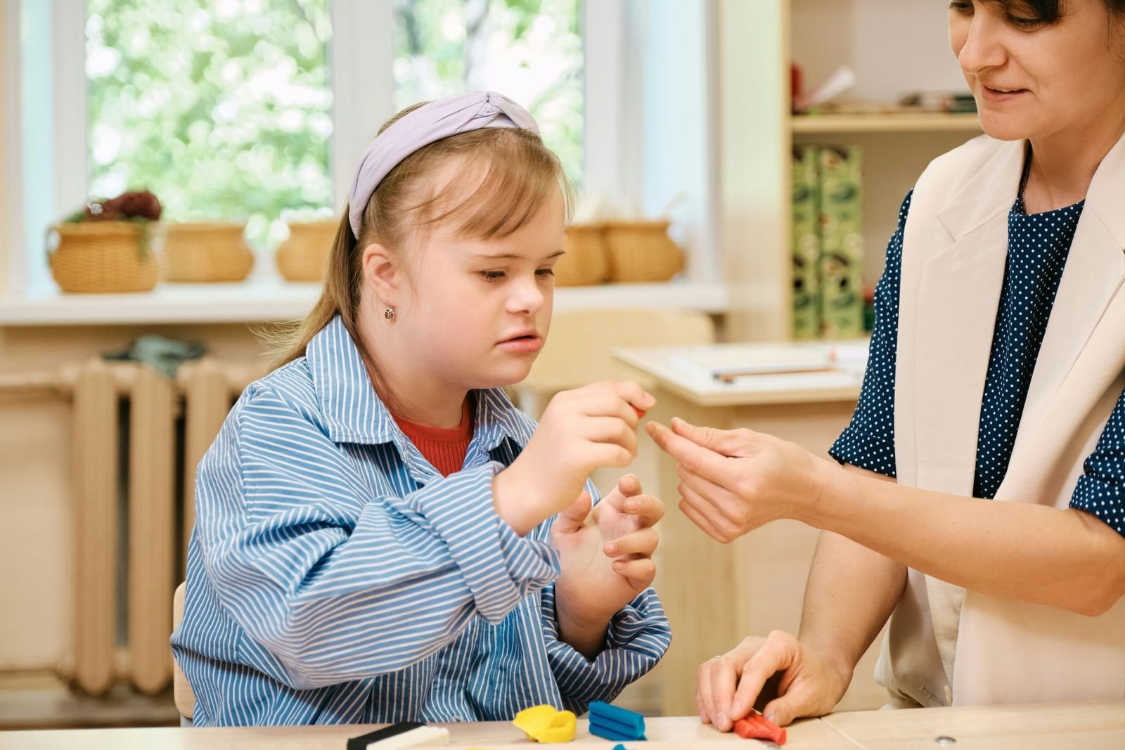 A therapist works hands-on with a young girl during a modeling clay activity