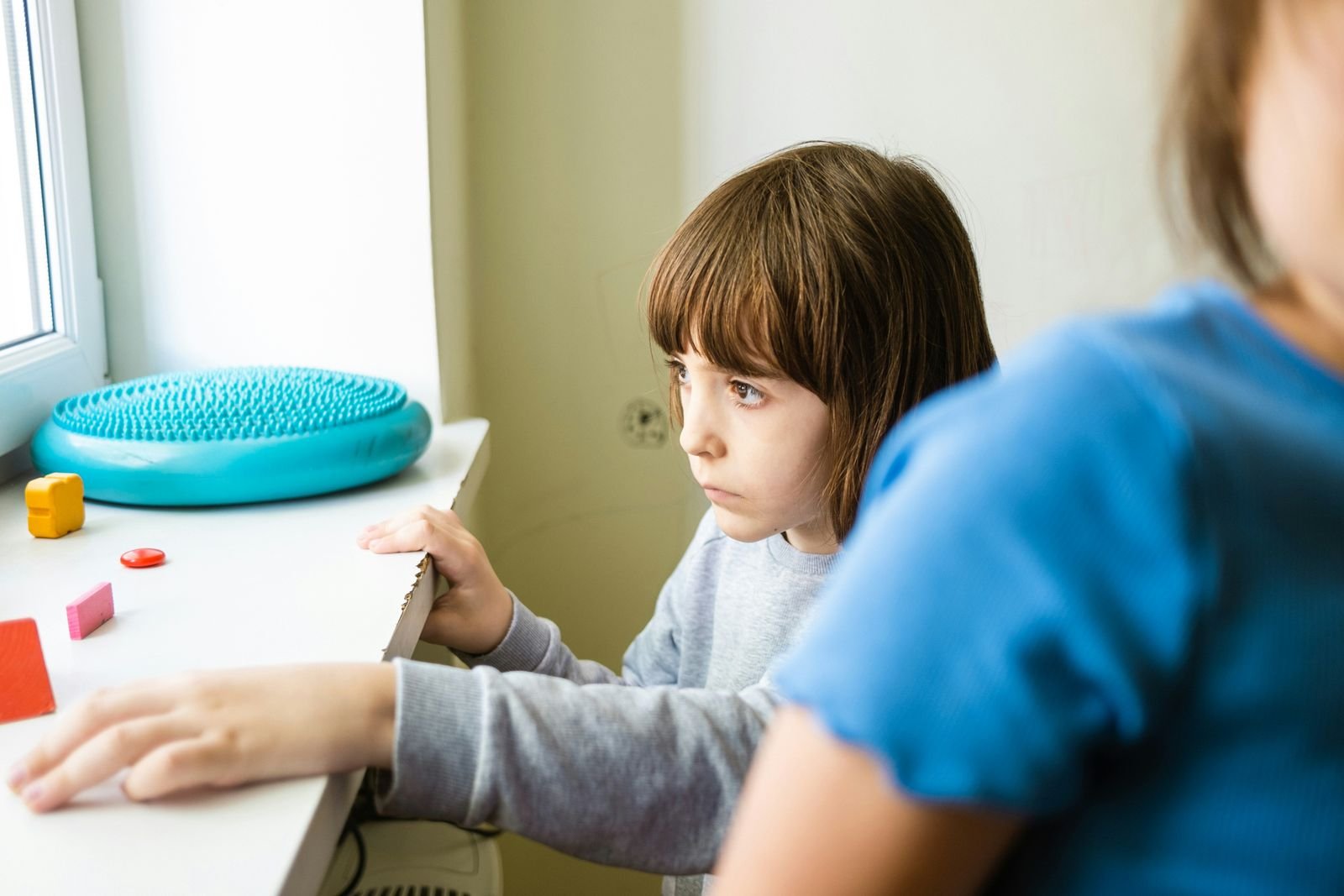 A clinician and a young child work together on a learning activity at a desk