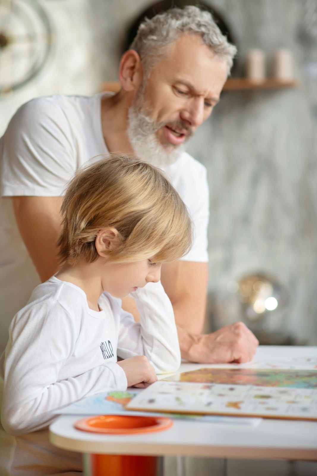 A grandfather and grandchild share a board game at the kitchen table