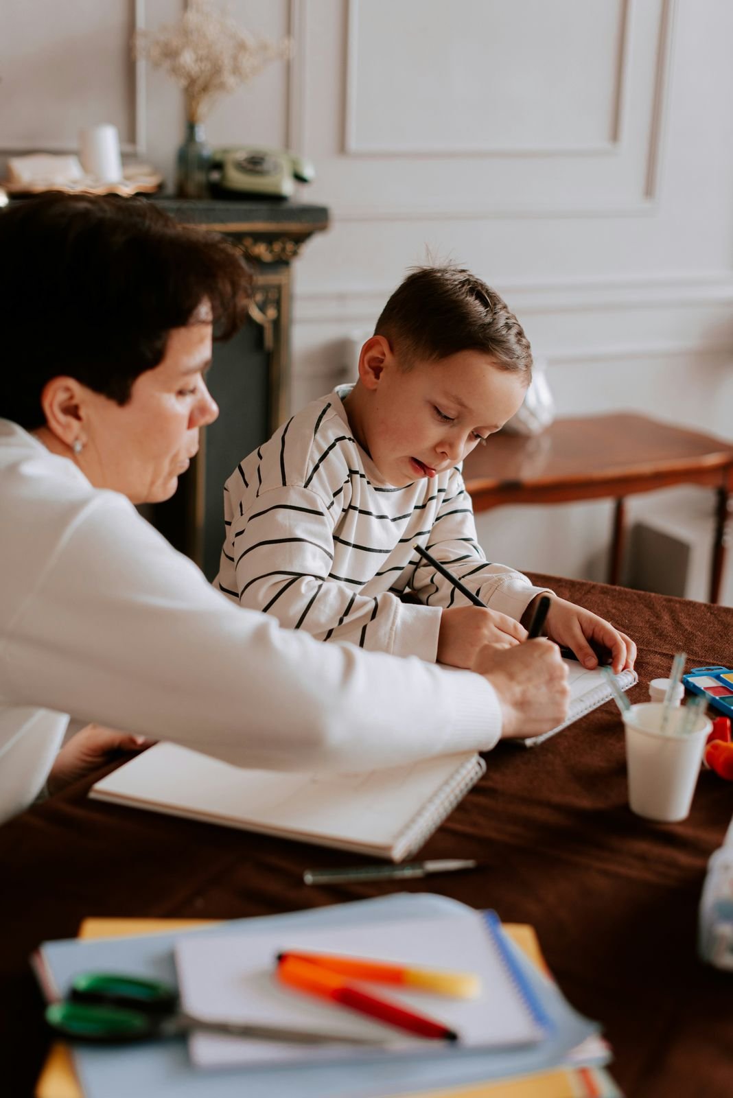 An adult guides a child through a writing activity at the family's kitchen table