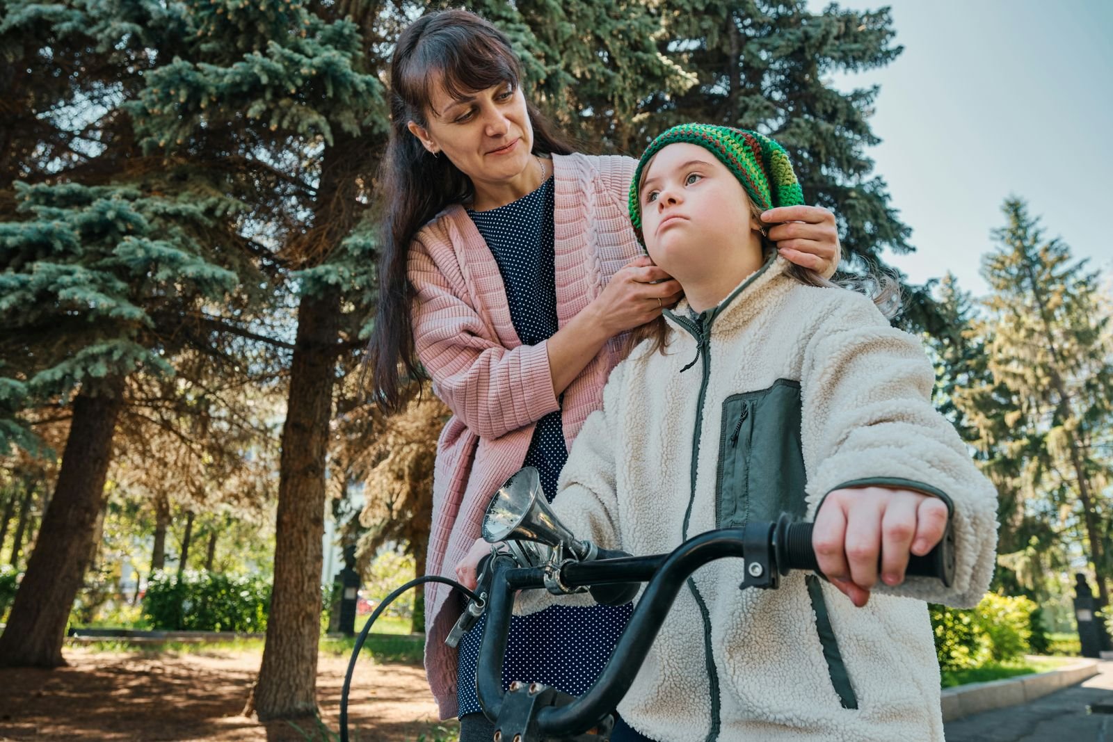 A mother adjusts her daughter's hat during a bike ride at the park