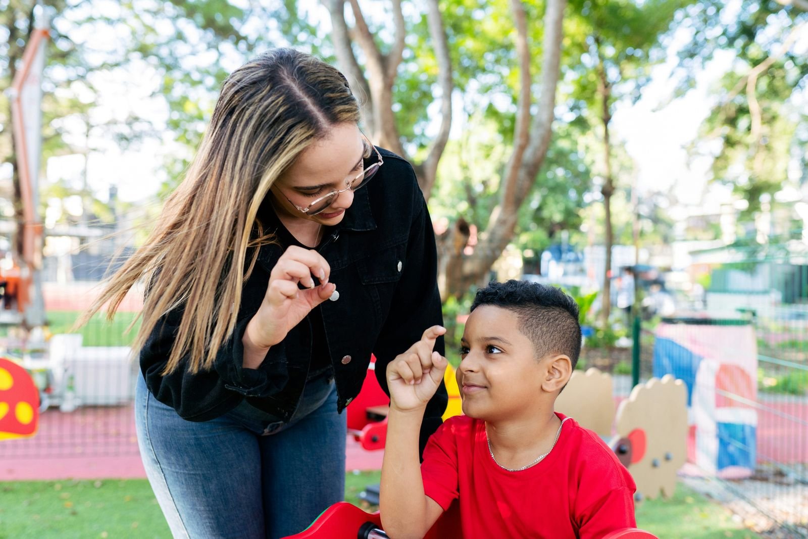 A technician and a smiling boy practice a hand game together at a neighborhood playground
