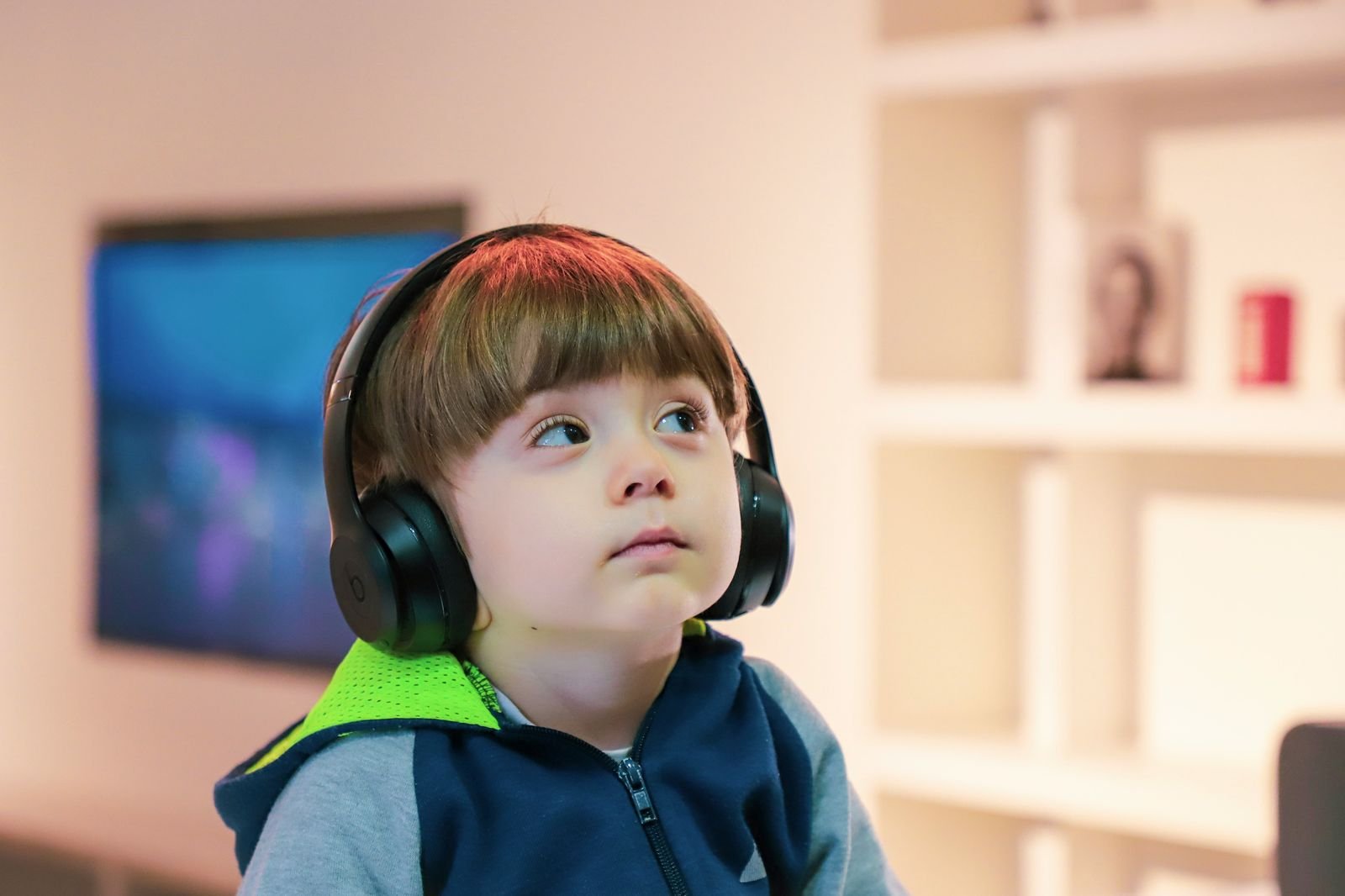 A toddler wearing headphones gazes upward with curiosity